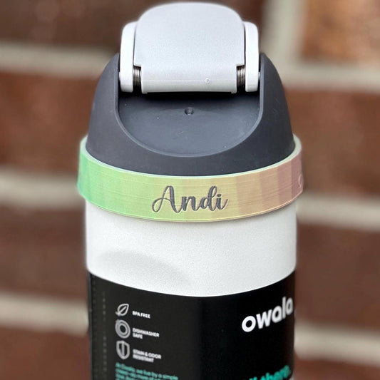 owala 24 oz freesip spout water bottle with a 3D printed ring with personalized name “Andi” round the top ring just below the lid.